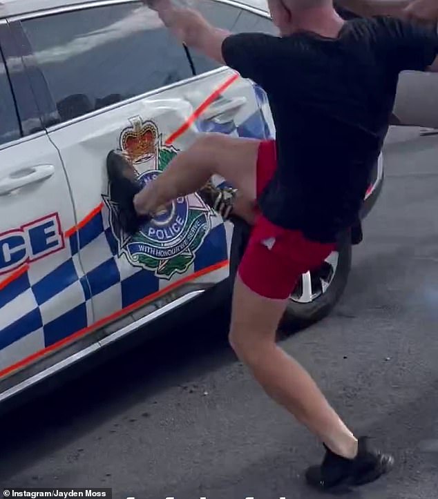 Officers and specialist units were called from the Logan, Gold Coast and South Brisbane districts to regain control of the fight (pictured, a man kicks a police car)