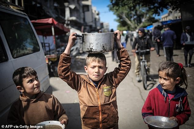 Children carry kitchen utensils as they walk towards a food distribution point in Gaza