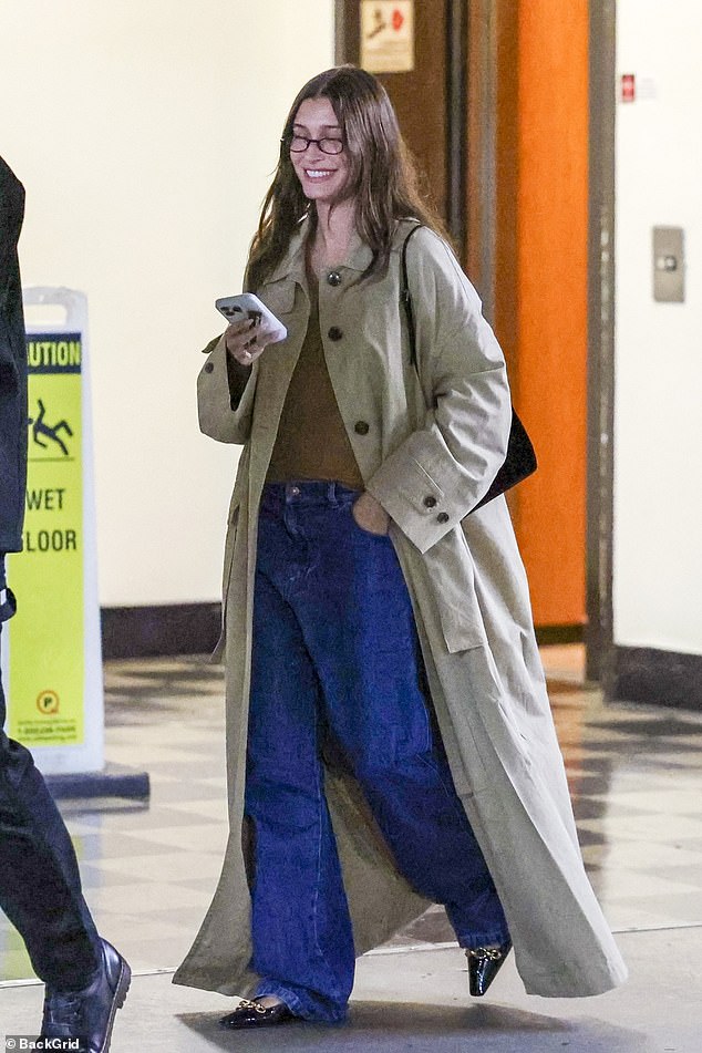 The model, 27, rocked a long beige trench coat over a brown top and flared jeans, but kept her ring finger hidden in her trouser pocket