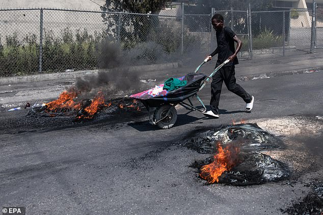 A person pushes a cart past tires set on fire by protesters during a protest in Port-au-Prince, Haiti, March 12, 2024