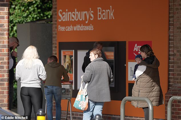 Customers are seen outside the Sainsbury's store in Lyons Farm, Worthington on Saturday, where the store only accepts cash.  Some appear to be withdrawing cash from the ATM.