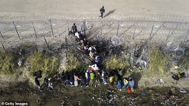 In an aerial view, immigrants walk through spools of razor wire while crossing the U.S.-Mexico border on March 13.