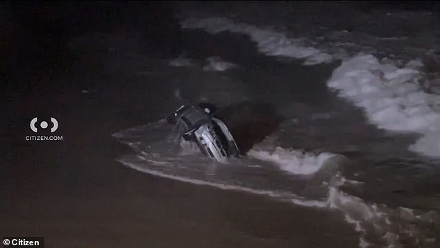 The car is seen bobbing in the waves after the woman, pursued by police, drove the vehicle over the sand and into the water.