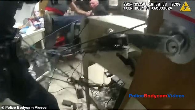 After more than 20 attempts, the door finally begins to give way, with officers coming face to face with the suspect - seen here rushing in with a hostage in tow as the two fall into a computer chair.