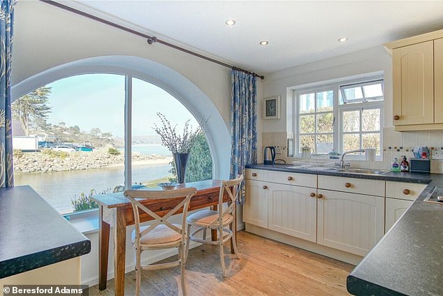 The kitchen has a country feel with cream cabinets and a large semi-circular window overlooking the water.