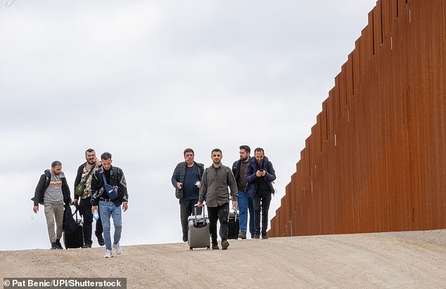 Migrants walk along the border wall with Mexico on the U.S. side last week to surrender to U.S. Border Patrol near Campo, California.  Biden highlighted Trump's comments on the migrant crisis and tough immigration policy in an interview on Univision radio.