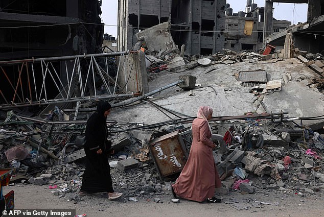 Women walk past a destroyed building in the southern Gaza town of Rafah following Israeli airstrikes