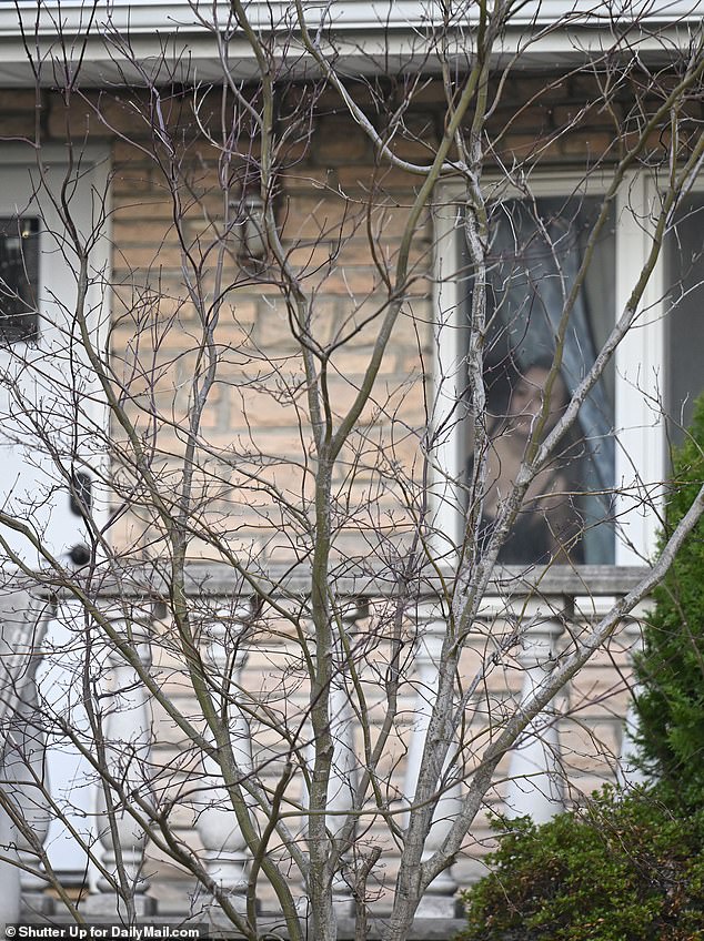 A woman crouching inside looks out the window to witness a confrontation.