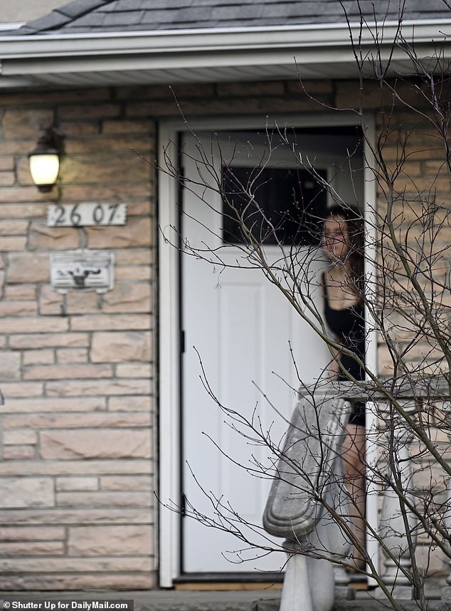 A woman, believed to be crouching in the house, peers through a crack in the front door.