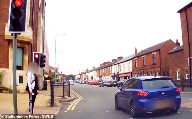 A video shows a blue car speeding past red lights as a person tries to cross the road.