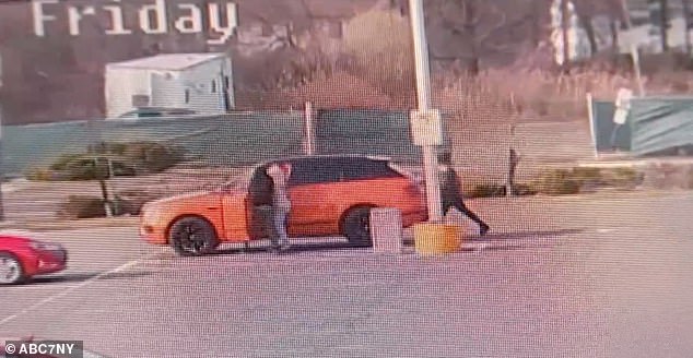 Two of the carjackers, one wearing a black hoodie and the other white, approach the driver directly while the third walks toward the passenger side.