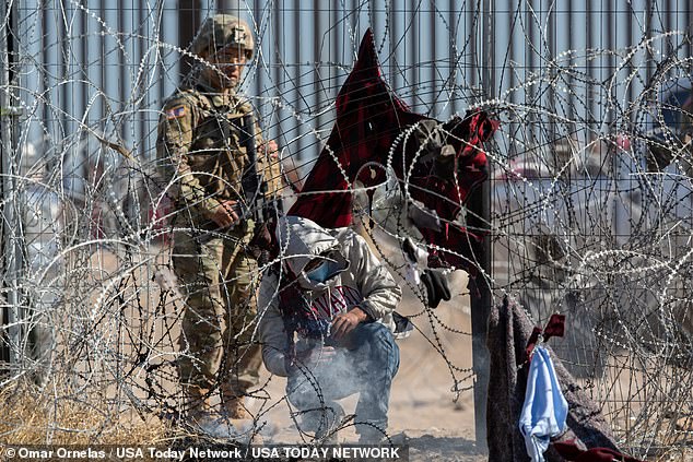 Male immigrants are escorted south behind a barrier by the Texas National Guard on the Rio Grande in El Paso, Texas, on March 21, 2024.