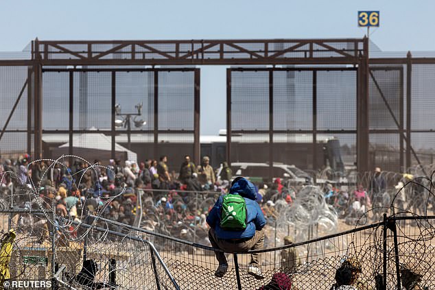 A migrant sits on a fence after a group of migrants broke through barbed wire and a fence.