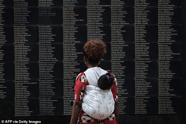 In this April 8, 2019 file photo, a woman carrying her child looks at the wall with the names of the victims as Rwanda marks the 25th anniversary of the 1994 genocide