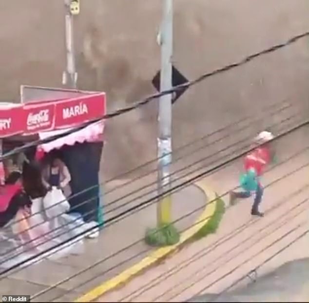 A city worker runs away from water pouring over a reservoir wall as people remained inside a shop in the Bolivian capital La Paz on Wednesday