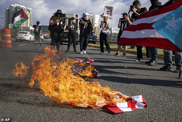 People take pictures of an American flag that was set on fire during a protest against the visit of US Vice President Kamala Harris