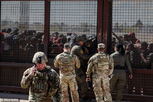 Members of the Texas National Guard work with Border Patrol to coordinate migrants who crossed the border from Mexico and made their way through barbed wire as they wait to be processed by border patrol while being detained on the U.S. side of the Rio Grande, in El Paso, Texas