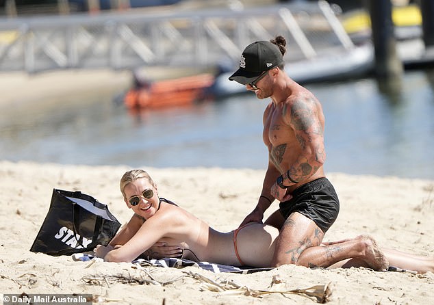 After swimming, the blonde lay down on a beach towel while Jack sat on top of her.