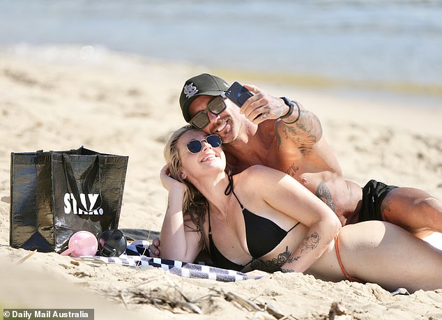 The couple smiled as they relaxed on the sand and posed for a selfie.