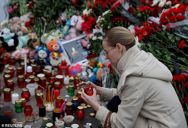 A woman lights a candle at a makeshift memorial to victims of a shooting attack set up outside the Crocus City Hall concert hall in Moscow region, Russia, on March 24.