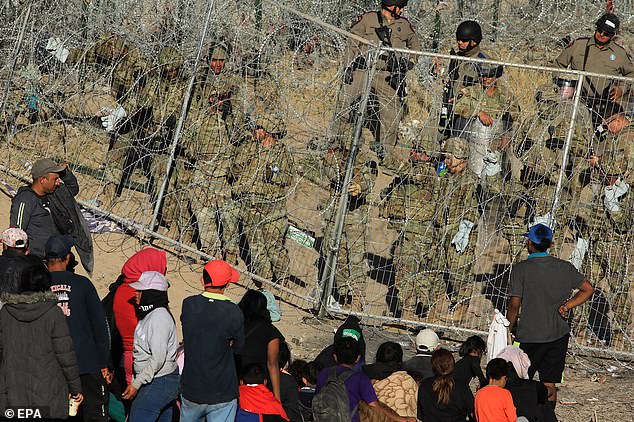 US National Guard personnel reinforce a fence covered with concertina wire in the vicinity of migrants on the border with Mexico, as seen from Ciudad Juárez