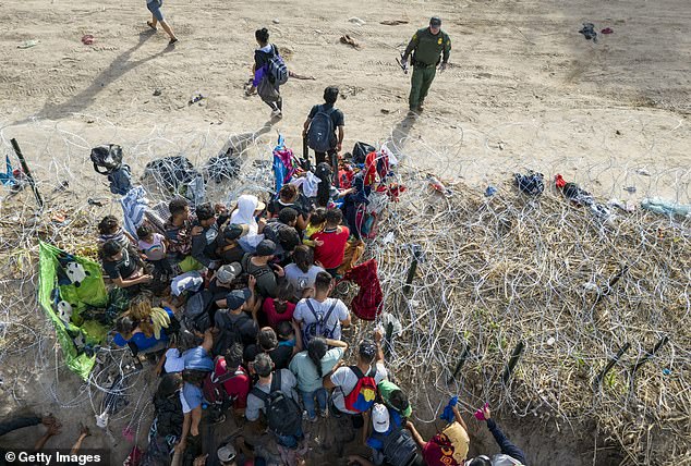 A U.S. Border Patrol agent monitors as migrants enter the United States after crossing the Rio Grande from Mexico on September 30, 2023 in Eagle Pass, Texas. The agent had cut coils of barbed wire to allow them to pass for processing.