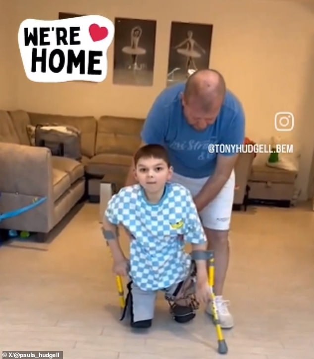 The nine-year-old bravely demonstrated his mobility skills and walked across his living room with his adoptive father (pictured)