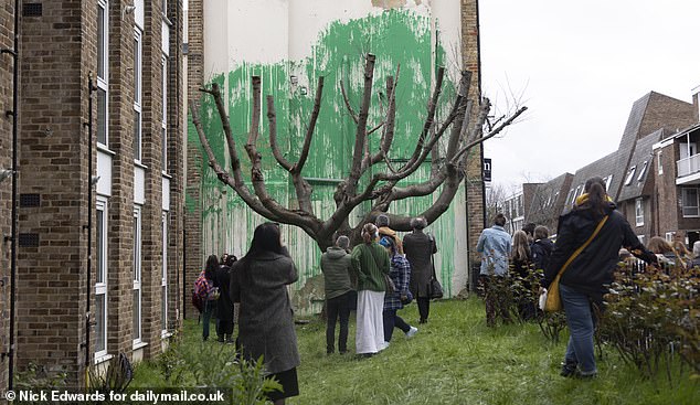 It was created with green paint behind a bare tree to resemble foliage, with a stencil of a person holding a pressure hose next to it.
