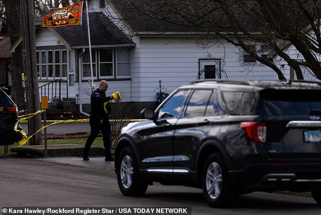 An officer deploys police tape Wednesday as the investigation into the quadruple homicide continues.
