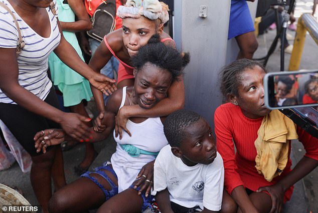 A woman is comforted by others at the crime scene where an ambulance was removing the bodies of several people, who were shot to death this morning amid escalating gang violence, in Port-au-Prince.