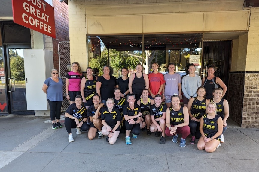 A team of netball players stands outside a cafe.