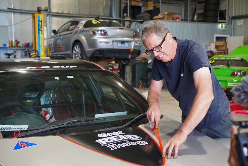 A man puts racing stripes on the hood of a car.
