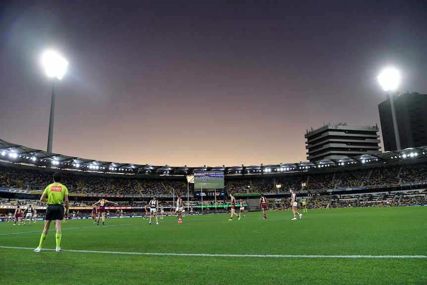 A general view of the Gabba hosting an AFL match with two lighting towers in operation.