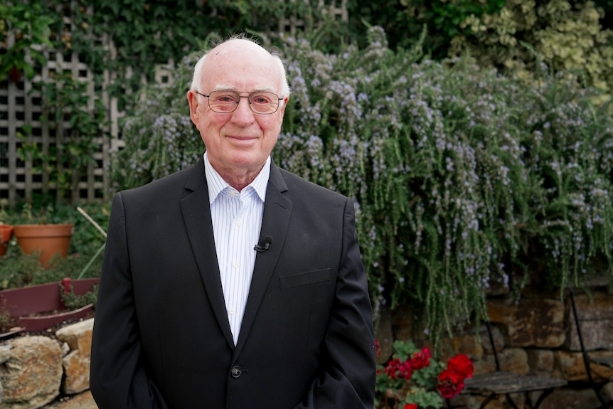 An elderly man with glasses and a suit in a garden patio