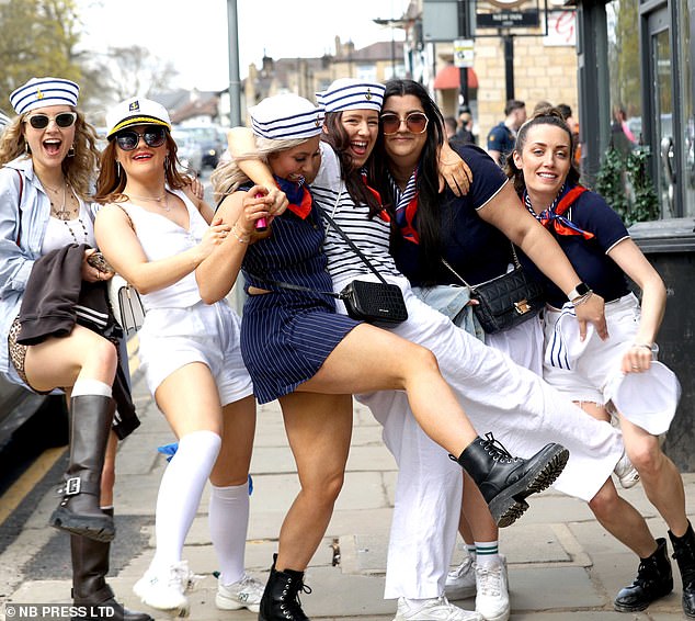 A group of friends are dressed as sailors while smiling and laughing. Some wear sunglasses for sunny weather.