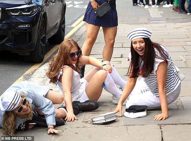 A group of friends laugh and smile after falling to the ground in the street