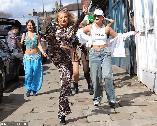 A girl does a high kick dressed as Scary Spice. In the background, you can see a girl dressed in an Arab costume while another girl is dressed in sportswear.