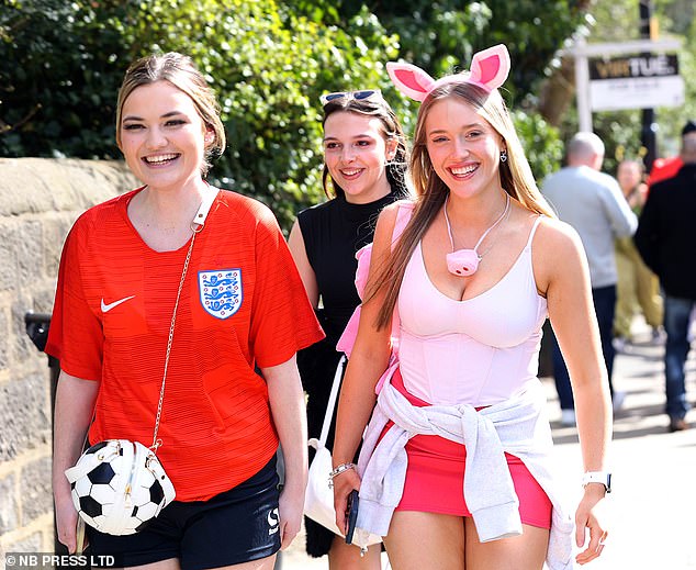 A girl dressed in an England kit smiles with her friend dressed as an Easter bunny and another girl with sunglasses on her head.