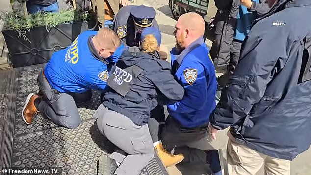 In the midst of the chaos, a bearded man wearing a brown hoodie was forcefully thrown to the ground by law enforcement officers, who proceeded to restrain his hands.