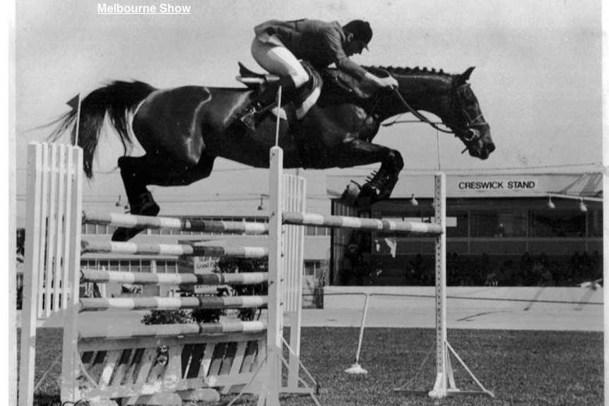 A black and white image of a rider jumping double oxer