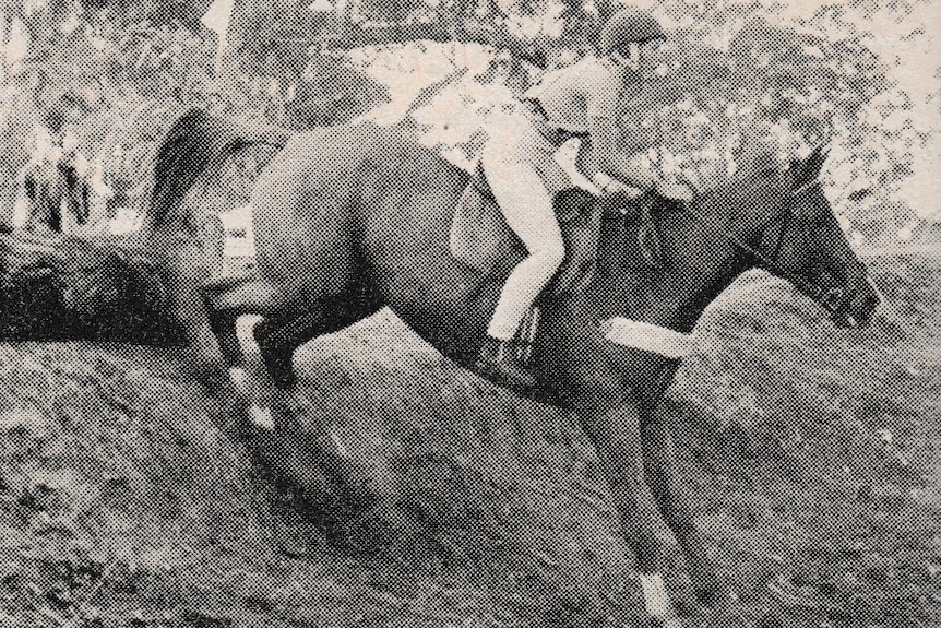 Black and white newspaper image of a rider and horse descending a steep embankment.