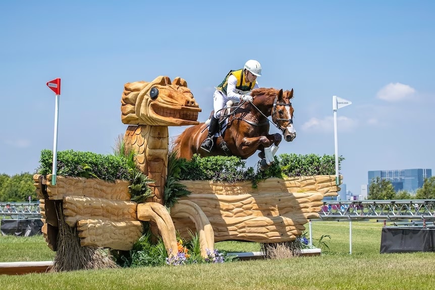 Olympic rider jumps a brown horse over an ornate background jump
