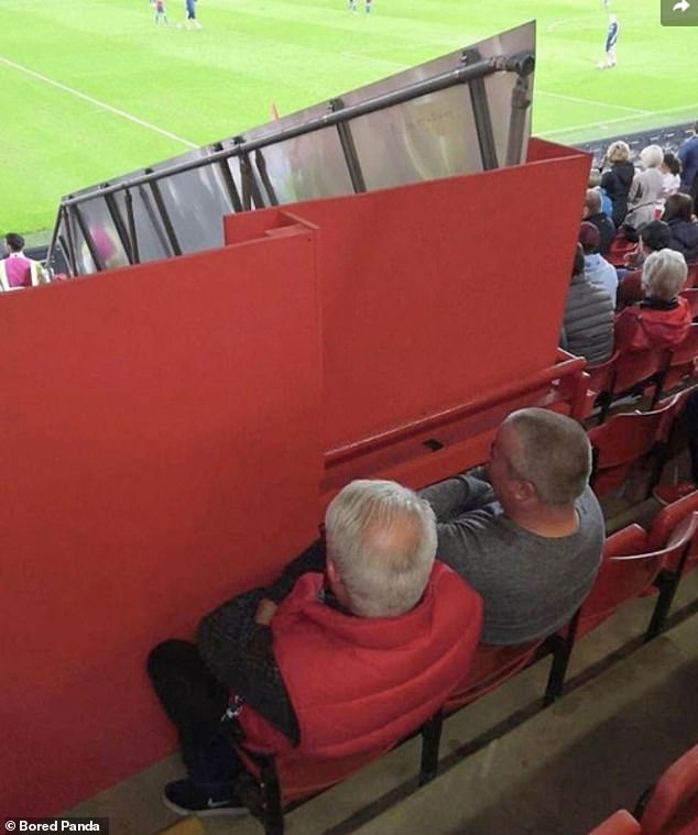 'Cheap seats' take on a new meaning here.  The two men may be in the stadium, but the solid fence means they can't see anything.