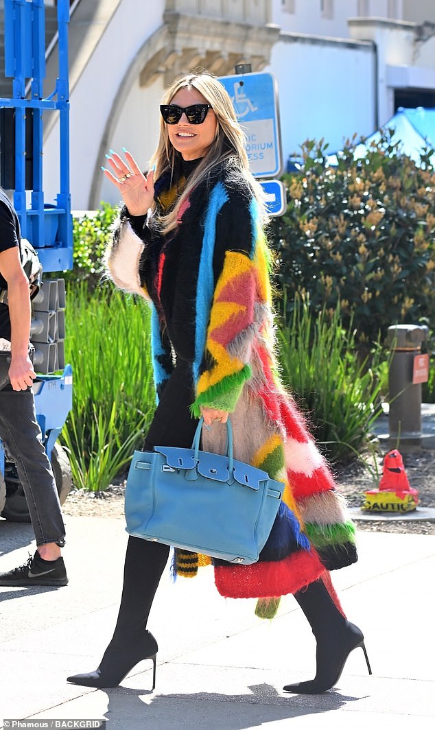 The fashionista also wore a pair of black stiletto boots, while carrying a blue handbag, which perfectly matched the blue of her rainbow jacket.