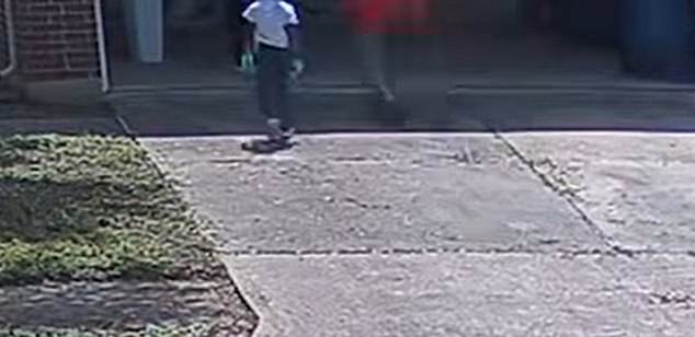 The boy in a red hoodie is seen pulling an object out of his pants and then running into the garage.