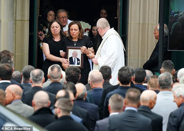 Mourners gather outside St.  Monica's Catholic Church in Moonee Ponds as family members walk outside with a photo of Latorre after the service