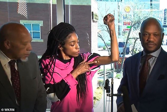 Ferguson, surrounded by her lawyers, raises her arm to show where one of the bullets hit her during the April 2023 incident.