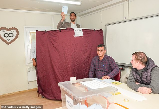 Sultan Kosen, who towers over everyone else in the world at 8ft 3in, was seen today peering through the privacy curtain at the polling station.