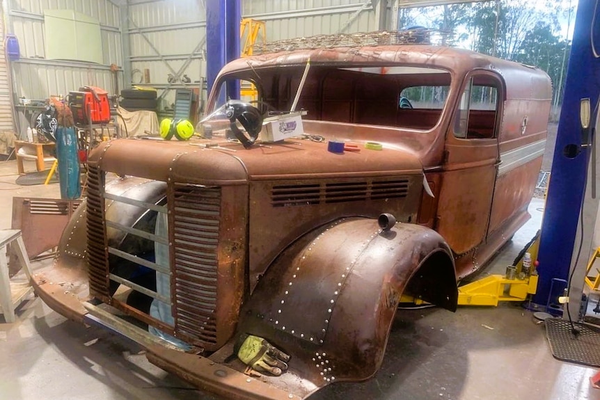 A rusty looking truck converted into a van in a backyard garage workshop.