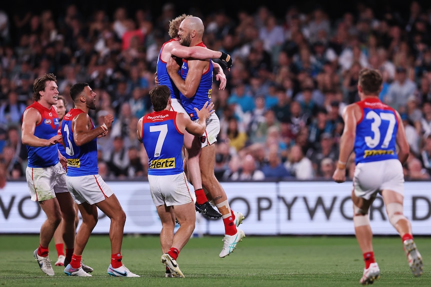 Melbourne's Max Gawn hugs in the air with a teammate as his team runs to congratulate him after a goal. 